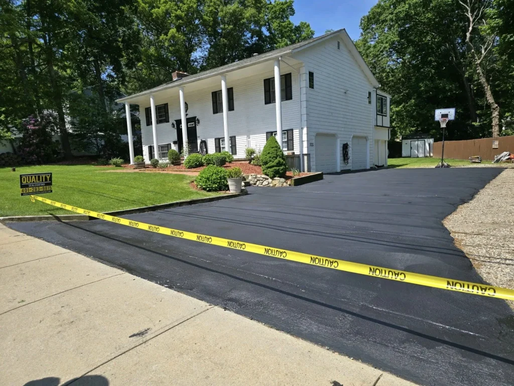 Newly sealcoated asphalt driveway with yellow caution tape in front of a house.